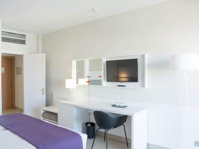 Helles, modernes Hotelzimmer mit weißem Schreibtisch, schwarzem Stuhl und Wandfernseher.