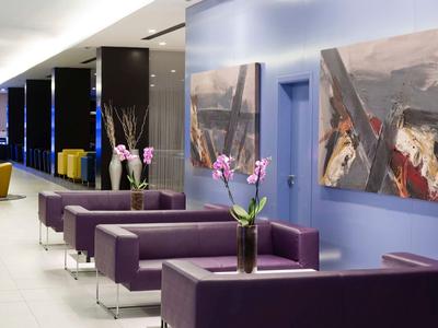 Moderner Wartebereich mit lila Sofas, blauen Wänden, Orchideen und abstrakten Gemälden.