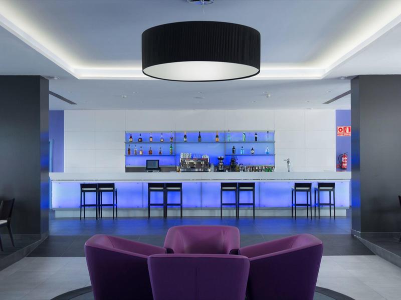Moderne hotelbar met blauw achtergrondlicht en paarse stoelen op de voorgrond.
