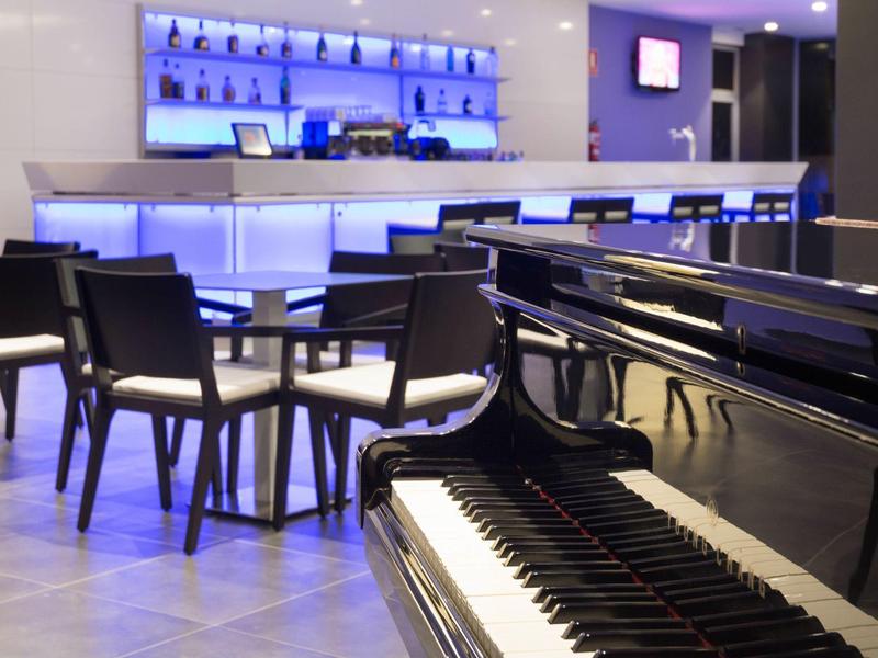 Moderne hotellounge met een strakke zwarte piano en bar met blauw licht op de achtergrond.