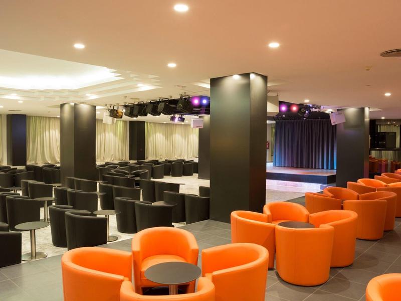 Moderne conferentiekamer met zwarte en oranje stoelen en een podium met verlichting.