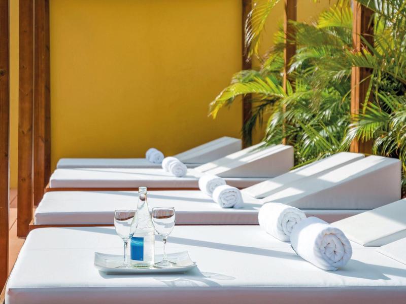 Witte ligstoelen met opgerolde handdoeken en een dienblad met glas water op een zonnig terras