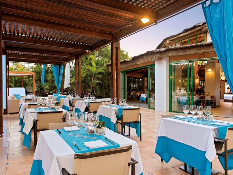 Buitenterras met turkooise en witte tafelkleden onder een houten pergola.