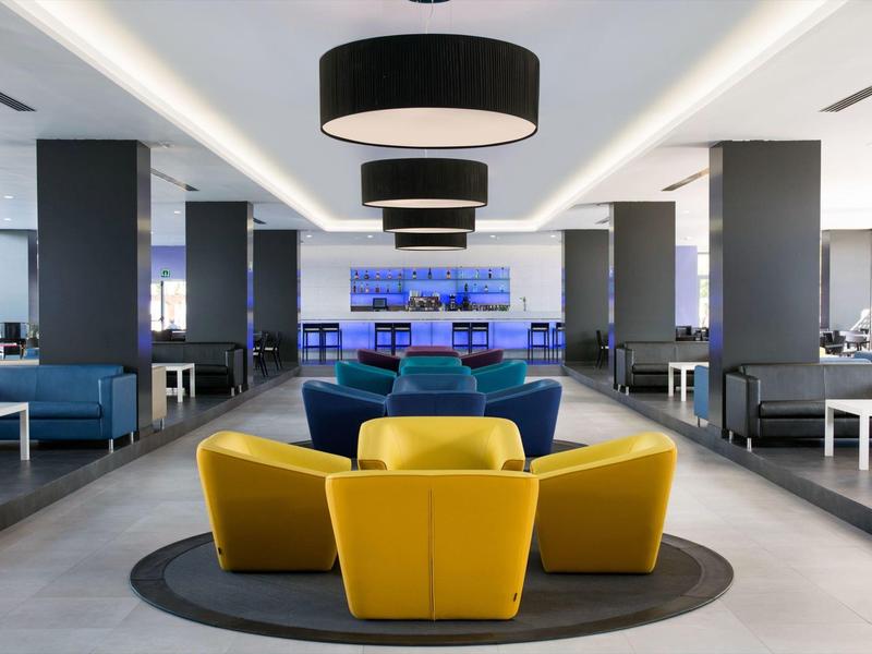 Moderne hotel lounge met gele stoelen en donkerblauwe banken rond een zwart vloerkleed.