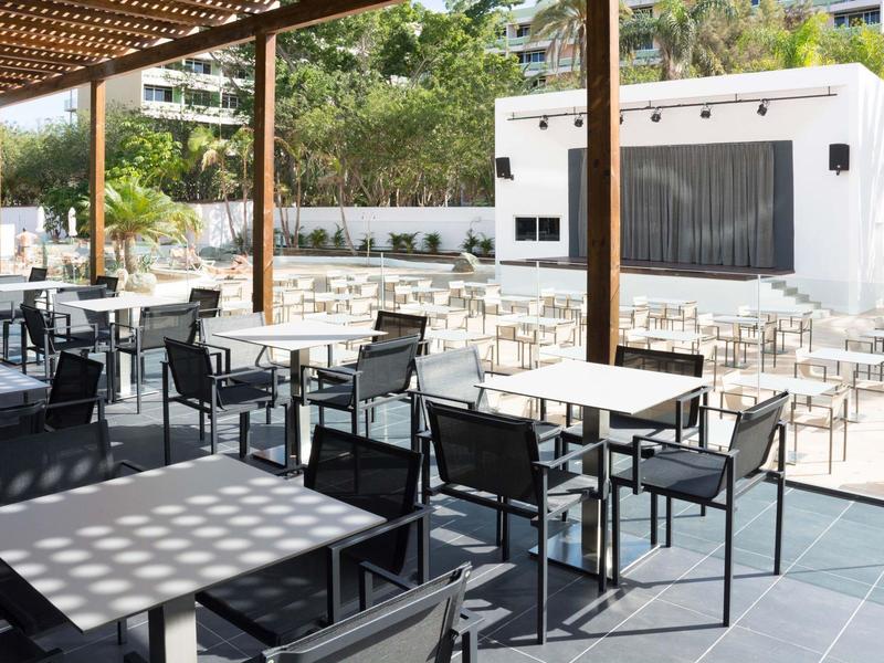 Buitenterras met tafels en stoelen onder een pergola en open lucht.