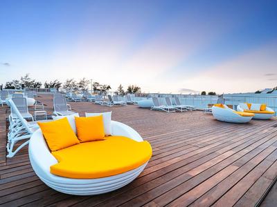 Fauteuils ronds modernes avec coussins orange sur une terrasse en bois sous un ciel bleu.