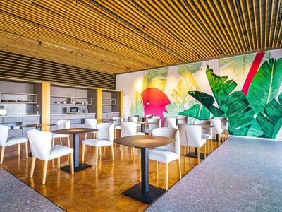 Nowoczesna restauracja z białymi krzesłami, drewnianą podłogą i kolorową dekoracją ścienną z motywami roślinnymi.