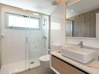 Jasna łazienka z przeszklonym prysznicem, toaletą i nowoczesną umywalką ze lustrem.