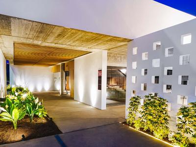 Nowoczesny korytarz hotelowy z oświetleniem, roślinami i białą ścianą z kwadratowymi otworami.