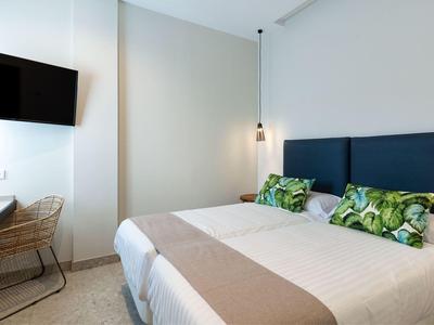 Prosty pokój hotelowy z dużym łóżkiem podwójnym, telewizorem na ścianie i małym biurkiem.