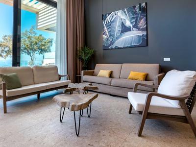 Nowoczesny salon z szarą sofą, fotelami i dekoracyjnym drewnianym stolikiem przy dużym oknie.