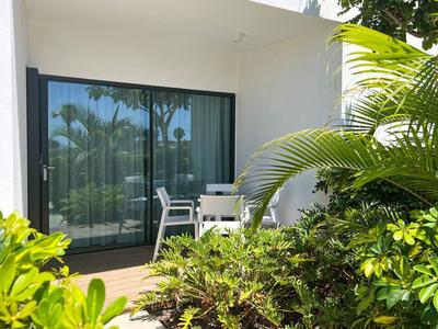 Prywatny taras z przesuwnymi drzwiami ze szkła, krzesłami i bujną zielenią przed pokojem hotelowym