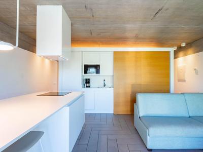 Nowoczesny hotelowy salon z niebieską sofą, białym aneksem kuchennym i otwartym designem.