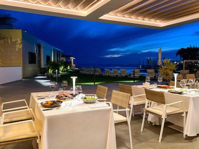 Abendliche Terrasse eines Hotels mit gedeckten Tischen, Blick auf Meer und Beleuchtung.