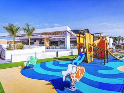 Kolorowy plac zabaw dla dzieci ze zjeżdżalnią i miejscami do siedzenia przed nowoczesnym hotelem.