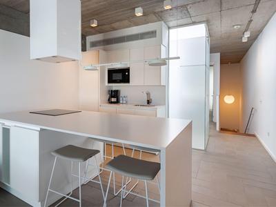 Nowoczesna, jasna kuchnia z białą wyspą, płytą grzewczą i dwoma stołkami w minimalistycznym stylu.