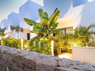 Nowoczesne białe budynki hotelowe z tropikalnymi roślinami i oświetleniem nocnym.