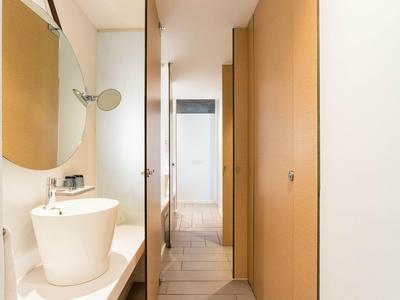 Nowoczesny korytarz hotelowy z białymi ścianami, drewnianymi drzwiami i umywalką z okrągłym lustrem.