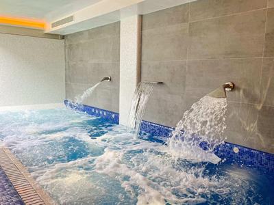 Basen kryty z dyszami do masażu wodnego i bulgoczącą wodą przy szarych kafelkach ściennych.