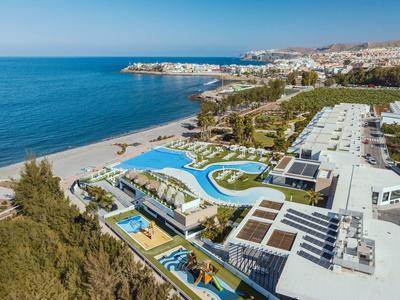 Zdjęcie z lotu ptaka ośrodka nadmorskiego z dużymi basenami, bezpośrednim dostępem do morza i rozległą piaszczystą plażą.