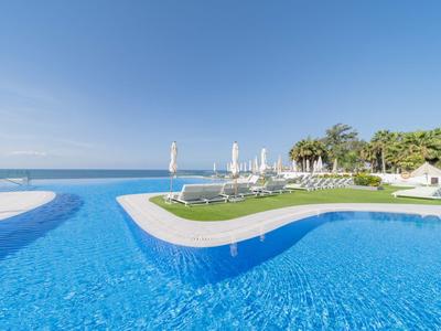 Moderner Pool mit klar blauem Wasser, Liegestühlen und Palmen am Meeresufer.