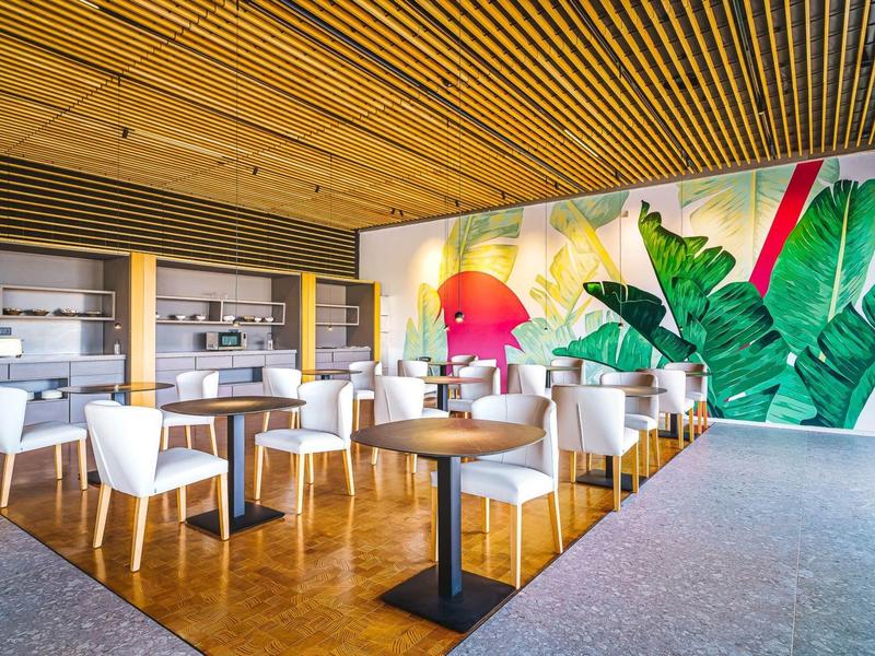 Nowoczesna restauracja z białymi krzesłami, drewnianą podłogą i kolorową dekoracją ścienną z motywami roślinnymi.