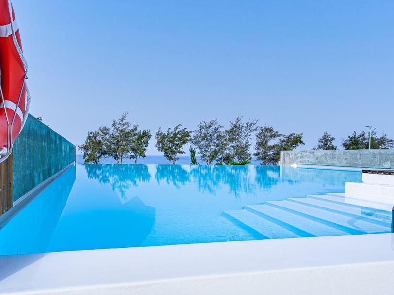 Nowoczesny basen infinity z czystą niebieską wodą i kołem ratunkowym na poręczy.