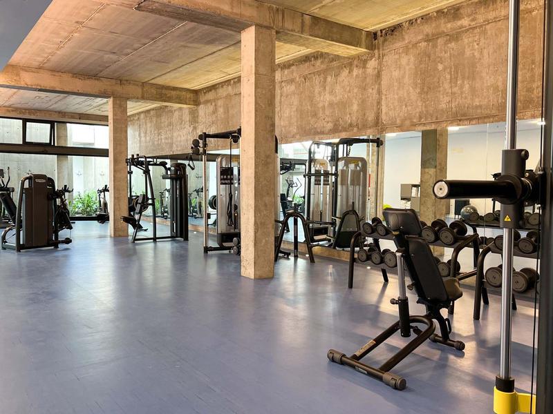 Nowoczesna siłownia z wyposażeniem w przestronnym pomieszczeniu z betonowymi ścianami i dużymi oknami.