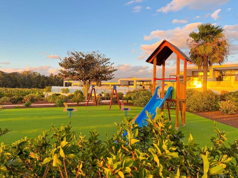 Plac zabaw z zjeżdżalnią i huśtawką w zadbanym ogrodzie o zachodzie słońca