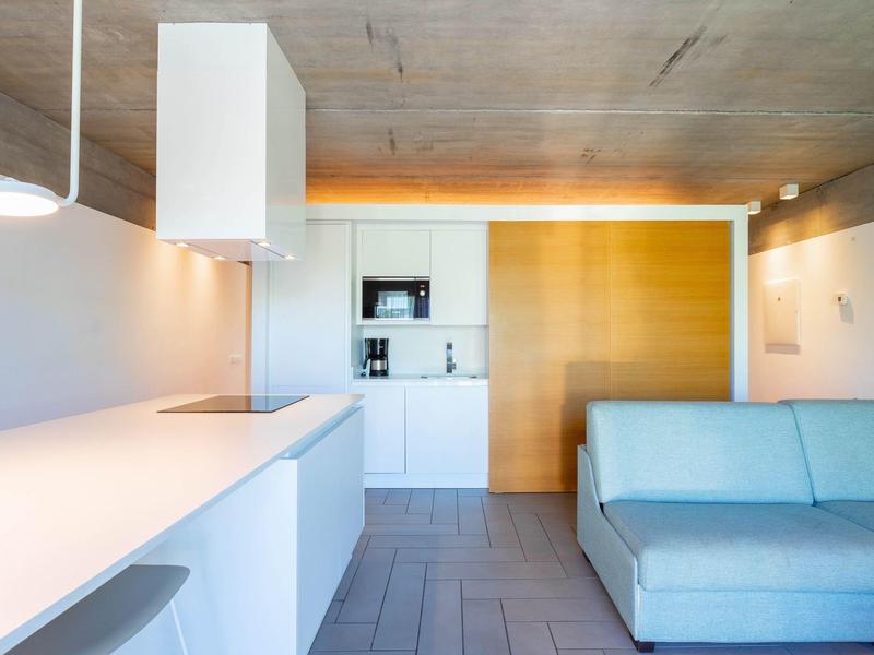 Nowoczesny hotelowy salon z niebieską sofą, białym aneksem kuchennym i otwartym designem.