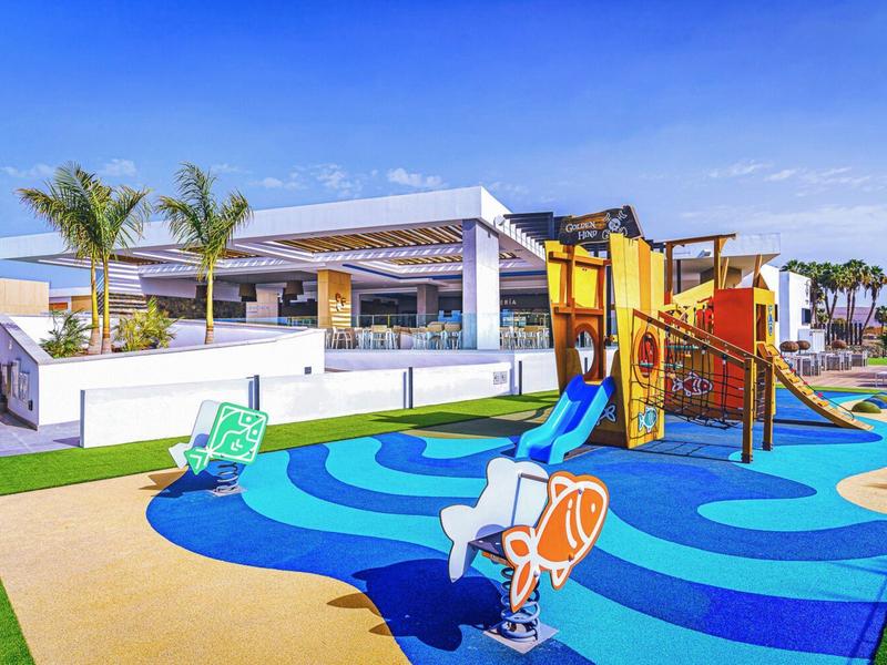 Kolorowy plac zabaw dla dzieci ze zjeżdżalnią i miejscami do siedzenia przed nowoczesnym hotelem.