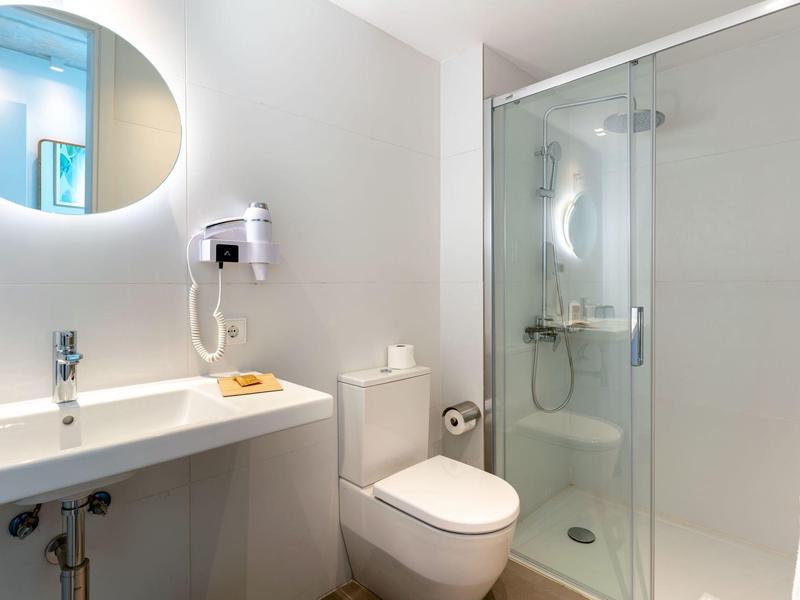 Nowoczesna łazienka z umywalką, toaletą, prysznicem i okrągłym lustrem.