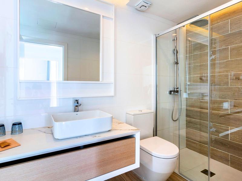 Jasna łazienka z umywalką, toaletą i prysznicem z szklanymi drzwiami i brązowymi kafelkami.