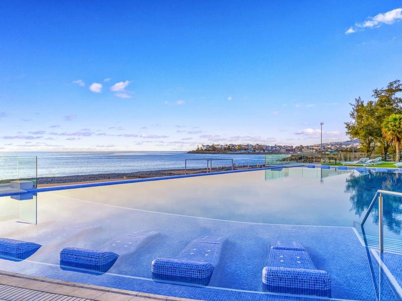 Basen infinity z niebieskimi leżakami z widokiem na morze pod czystym niebem.