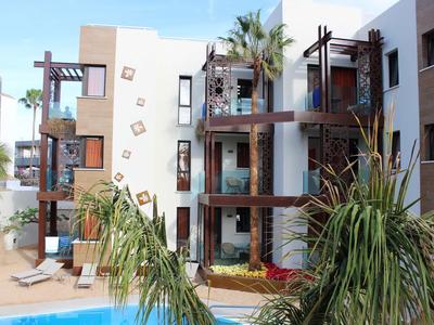 Modern hotel complex with multiple floors, balconies, and a pool in the foreground.