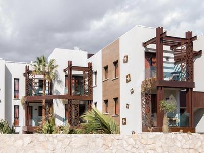 Modernes Hotelgebäude mit Balkonen und Palmen unter bewölktem Himmel.