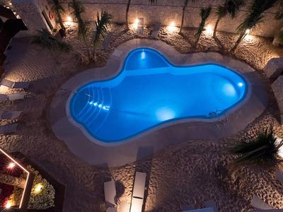 Beleuchteter Pool in organischer Form mit Umgebung aus Steinen und Pflanzen bei Nacht.