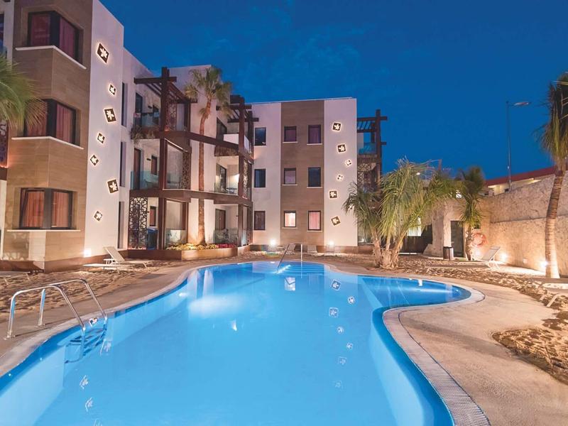 Illuminated outdoor hotel pool at night with lounge chairs and palm trees.