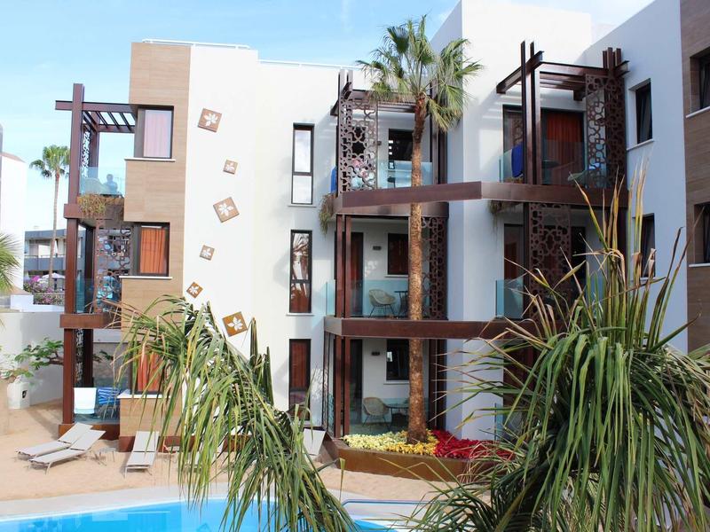 Modern hotel complex with multiple floors, balconies, and a pool in the foreground.