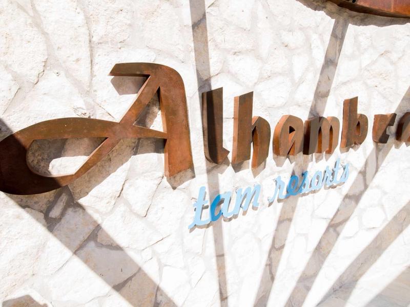 Metal Alhambra sign on white stone wall with shadows