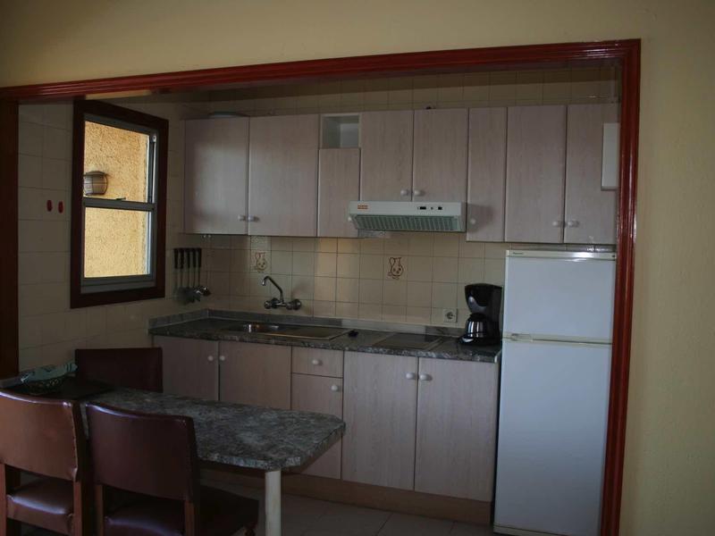 Kleine Küchenzeile mit hellen Schränken, Kühlschrank, Kaffeemaschine und zwei Stühlen am Tresen.