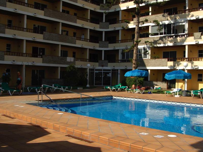 Innenhof eines Mehrfamilienhauses mit rechteckigem Swimmingpool und grün-blauen Liegestühlen.