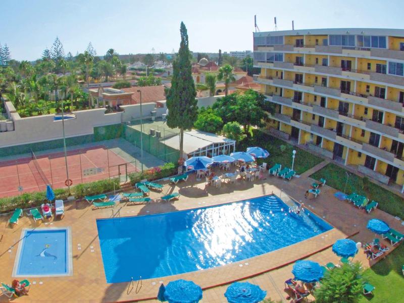 Ein Schwimmbad mit Sonnenschirmen und Liegestühlen neben einem mehrstöckigen Hotelgebäude.