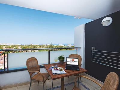 Balcony with table, three chairs, and city view under clear sky.