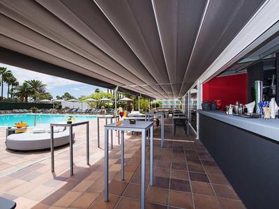 Modern outdoor area with bar, high tables, and pool view in a vacation resort atmosphere.