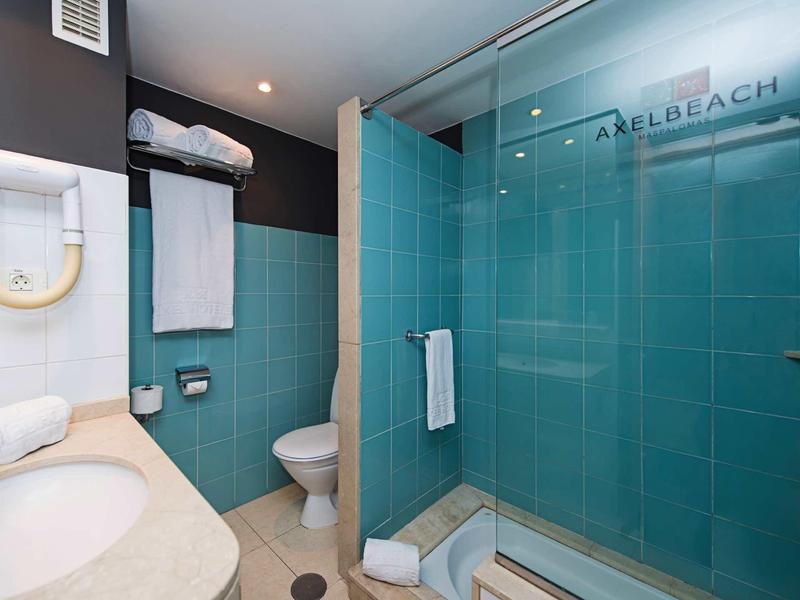 Modern bathroom with blue tiles, shower, toilet, and towels in a hotel room.