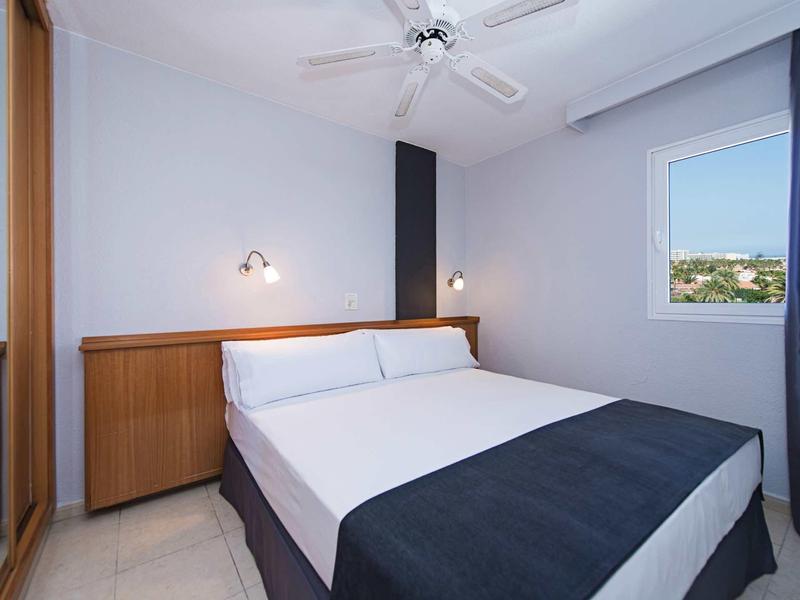 Modern hotel room with double bed, white walls, and large window with a view.