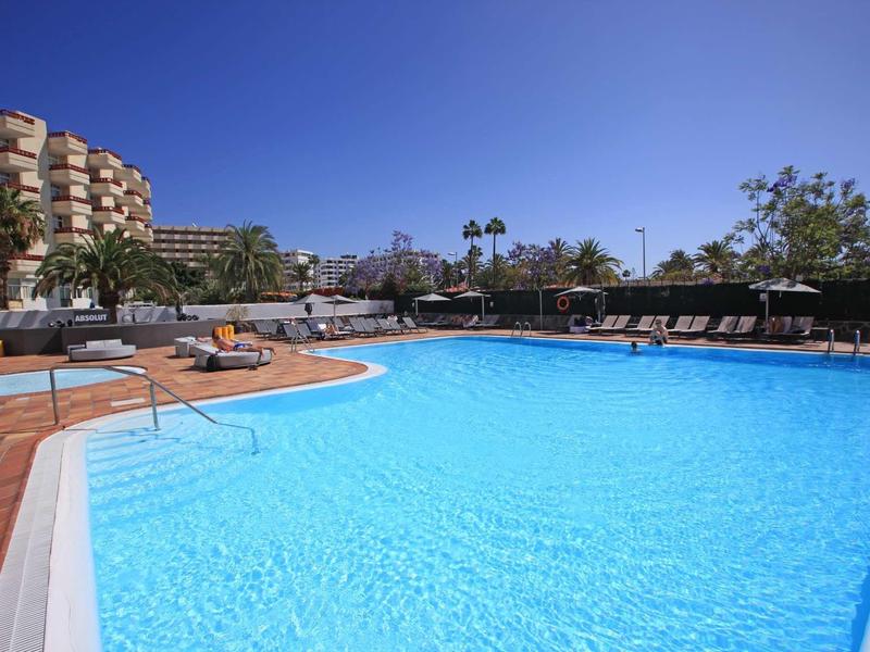 Large outdoor pool with blue water surface and sun loungers next to a hotel building.