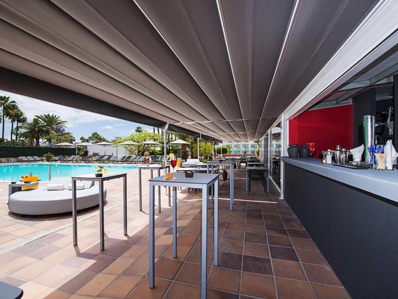 Modern outdoor area with bar, high tables, and pool view in a vacation resort atmosphere.