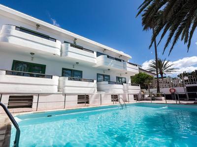 Modern white hotel building with balconies and clear outdoor pool under blue sky